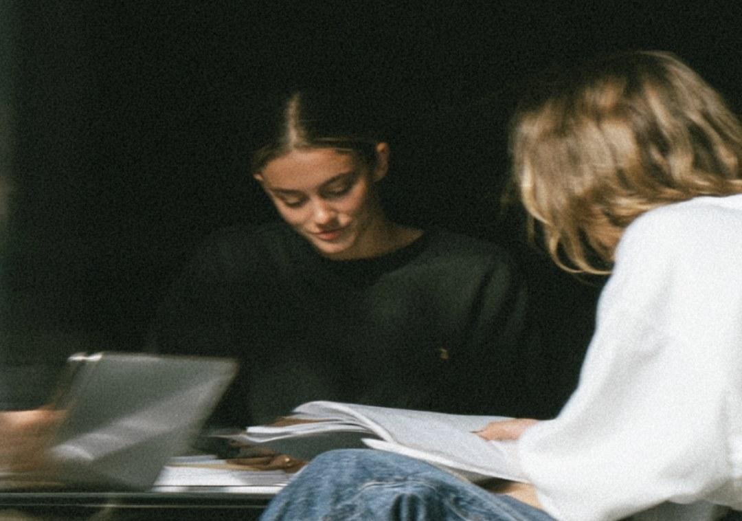 Two students working side by side over notes and a laptop