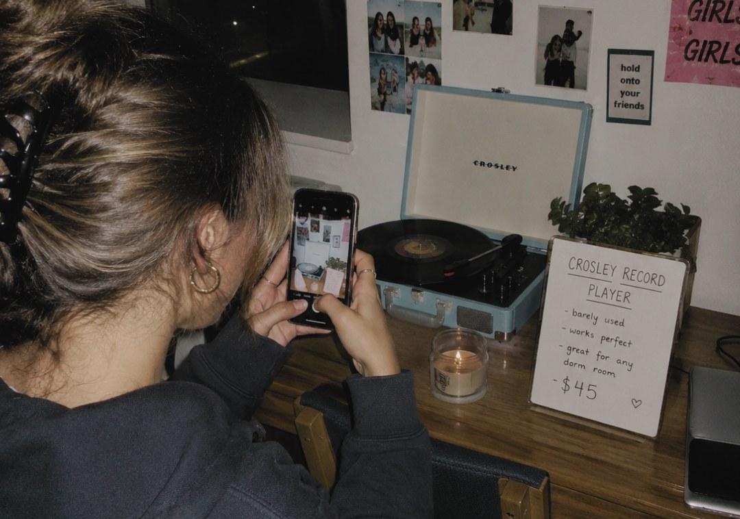 A student photographing a record player for sale beside a handwritten price card