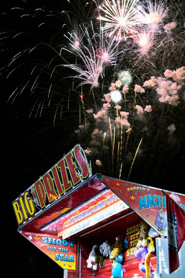 Fireworks bursting over a fairground stall at night